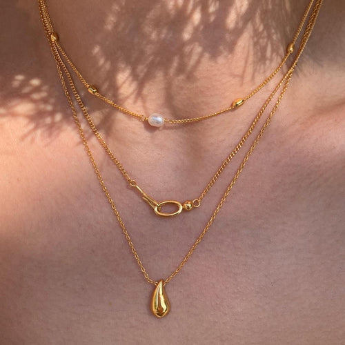 Two gold necklaces with pendant drops on a skin background